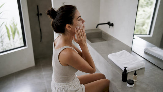 O femeie își masează fața cu un exfoliant, bucurându-se de un ritual de îngrijire într-o baie amenajată modern.