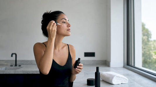 O femeie își aplică serul pe față, bucurându-se de lumina naturală din baie.